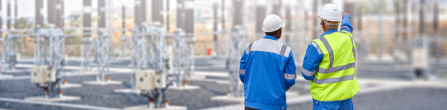 Engineers in safety gear inspecting equipment at a substation or power facility