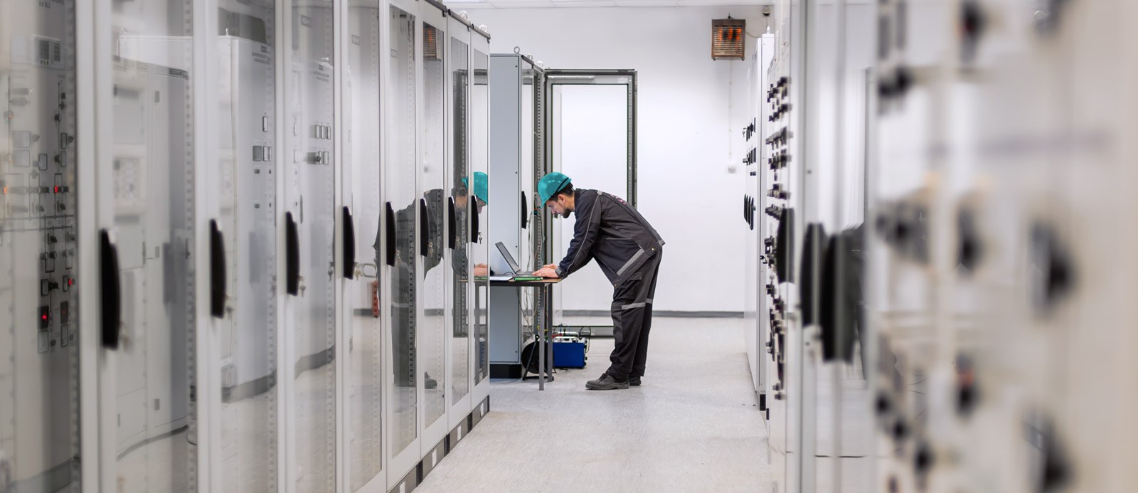 Technician using a laptop in a control room, monitoring or maintaining industrial systems